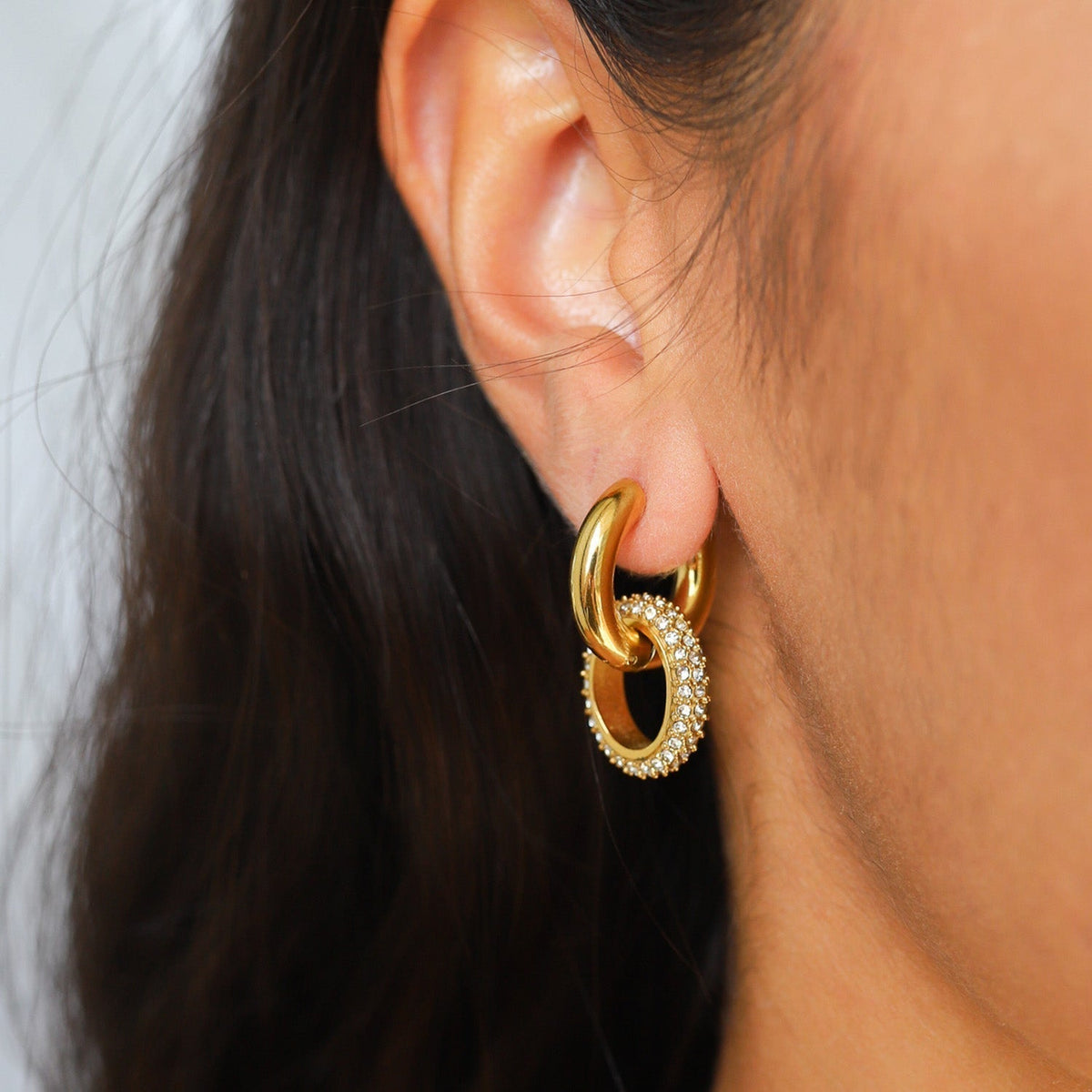 Gold-colored double hoop earrings with smooth and textured interlocking rings on a plain background